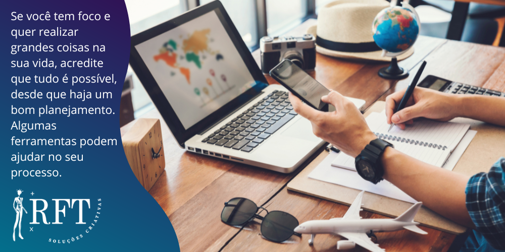Pessoa segurando um celular e escrevendo num caderno com uma caneta. Na mesa tem um notebook, um óculos, uma câmera fotográfica, um chapéu, um relógio despertador, uma calculadora, uma miniatura de avião, e uma descrição sobre ferramentas de planejamento para fazer realizações. 
